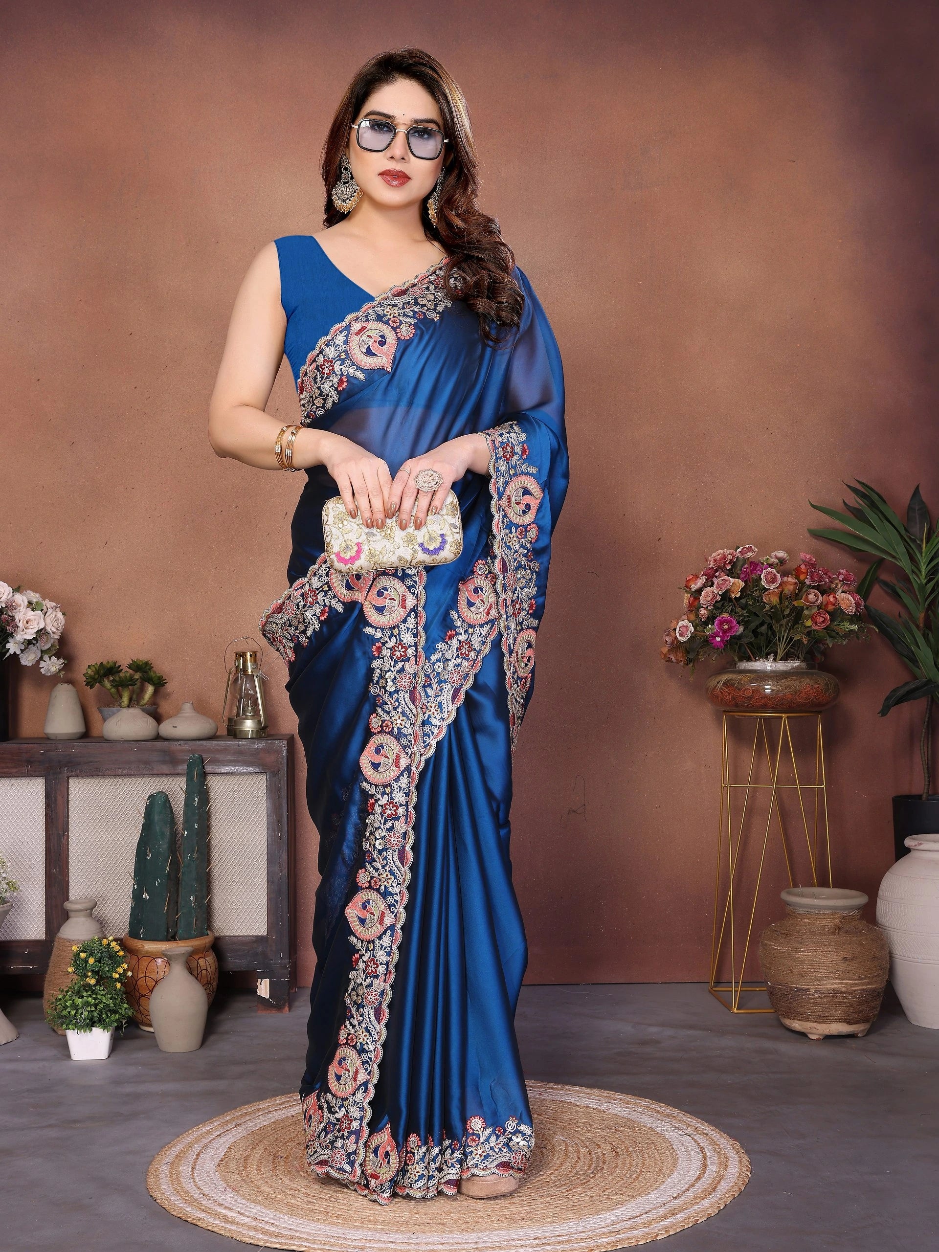 Woman in a blue saree with floral patterns standing in a decorated room.